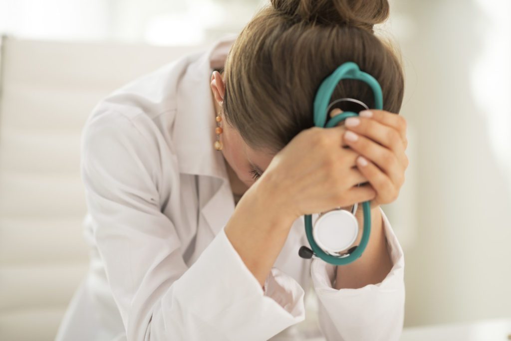 woman doctor with her head down in her hands worried and stressed